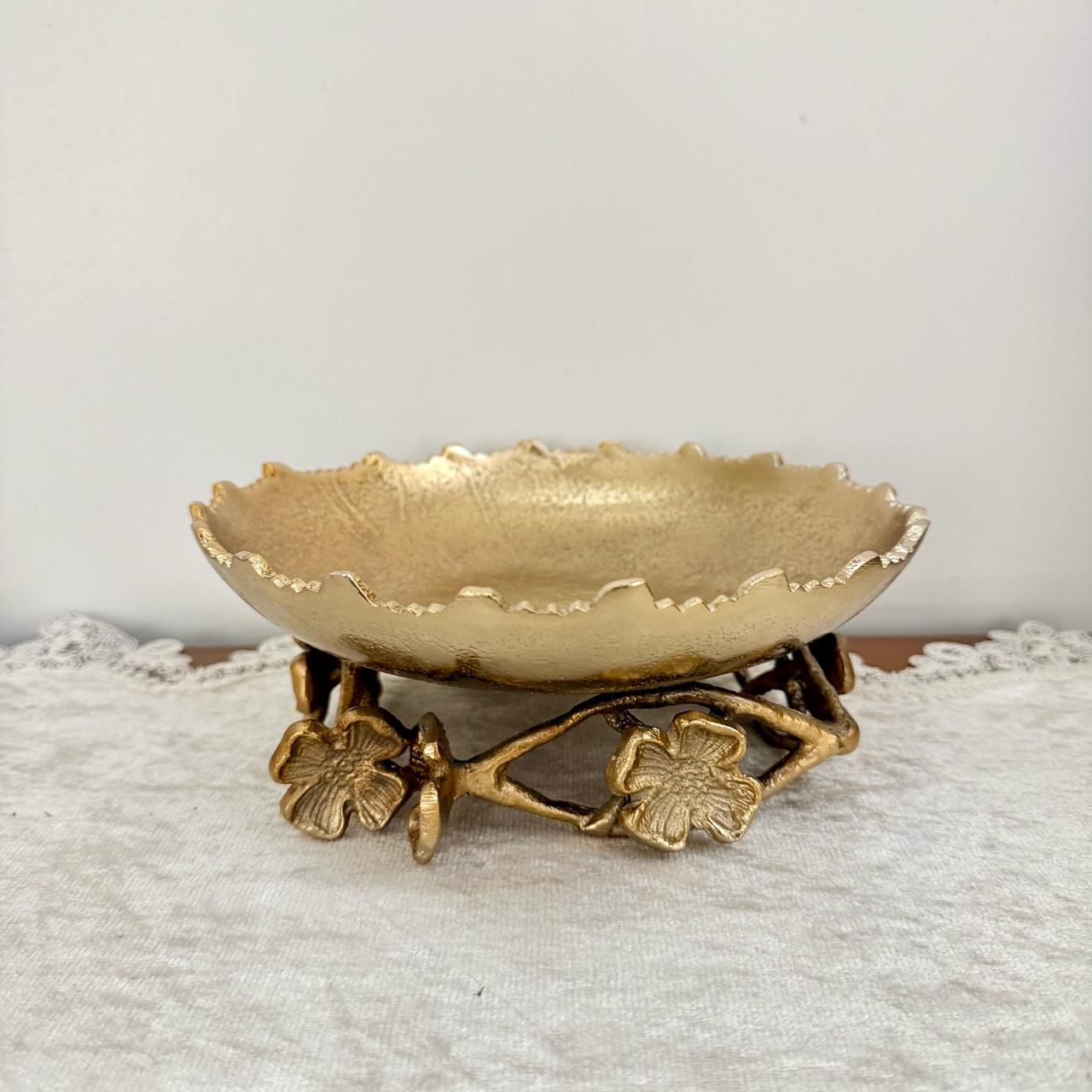 Decorative gold bowl on a matching stand with floral designs against a light background