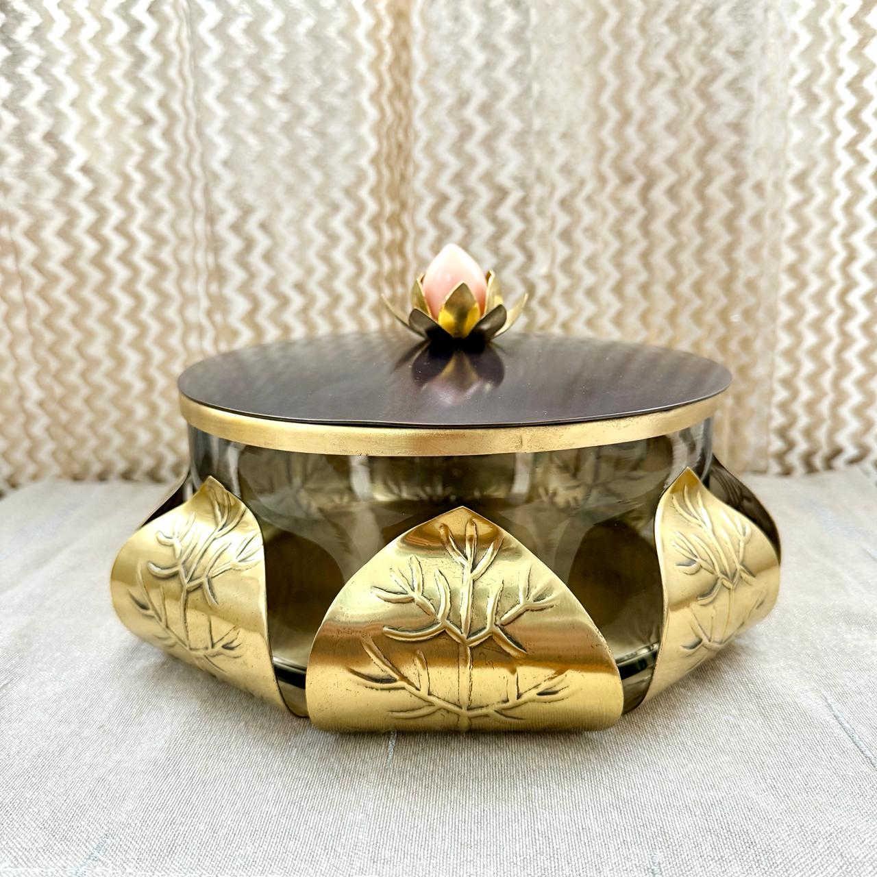 Decorative metal container with gold accents and a black lid on a textured surface.