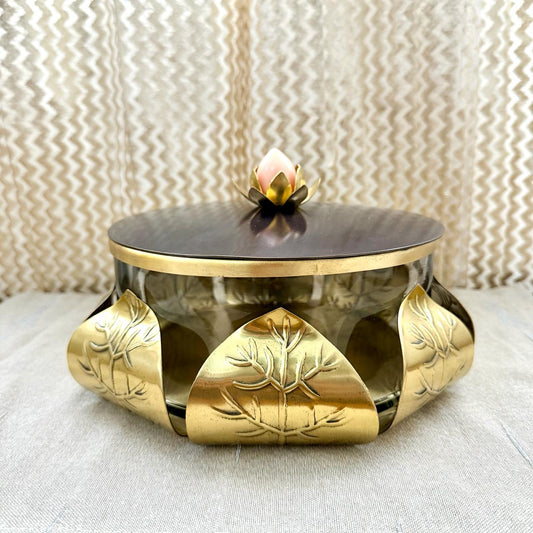 Decorative metal container with gold accents and a black lid on a textured surface.
