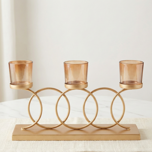 Gold candle holder with three glass candles on a white surface